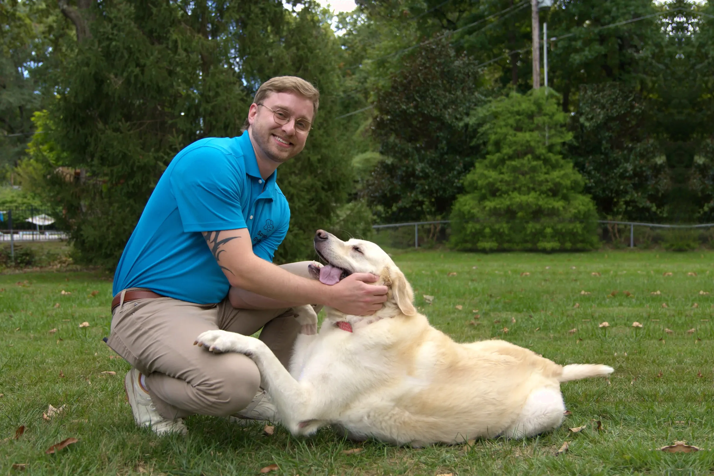 Scoop Group dog waste removal owner Zane Creek petting a happy yellow Labrador on a freshly mowed backyard lawn in Maplewood, MO